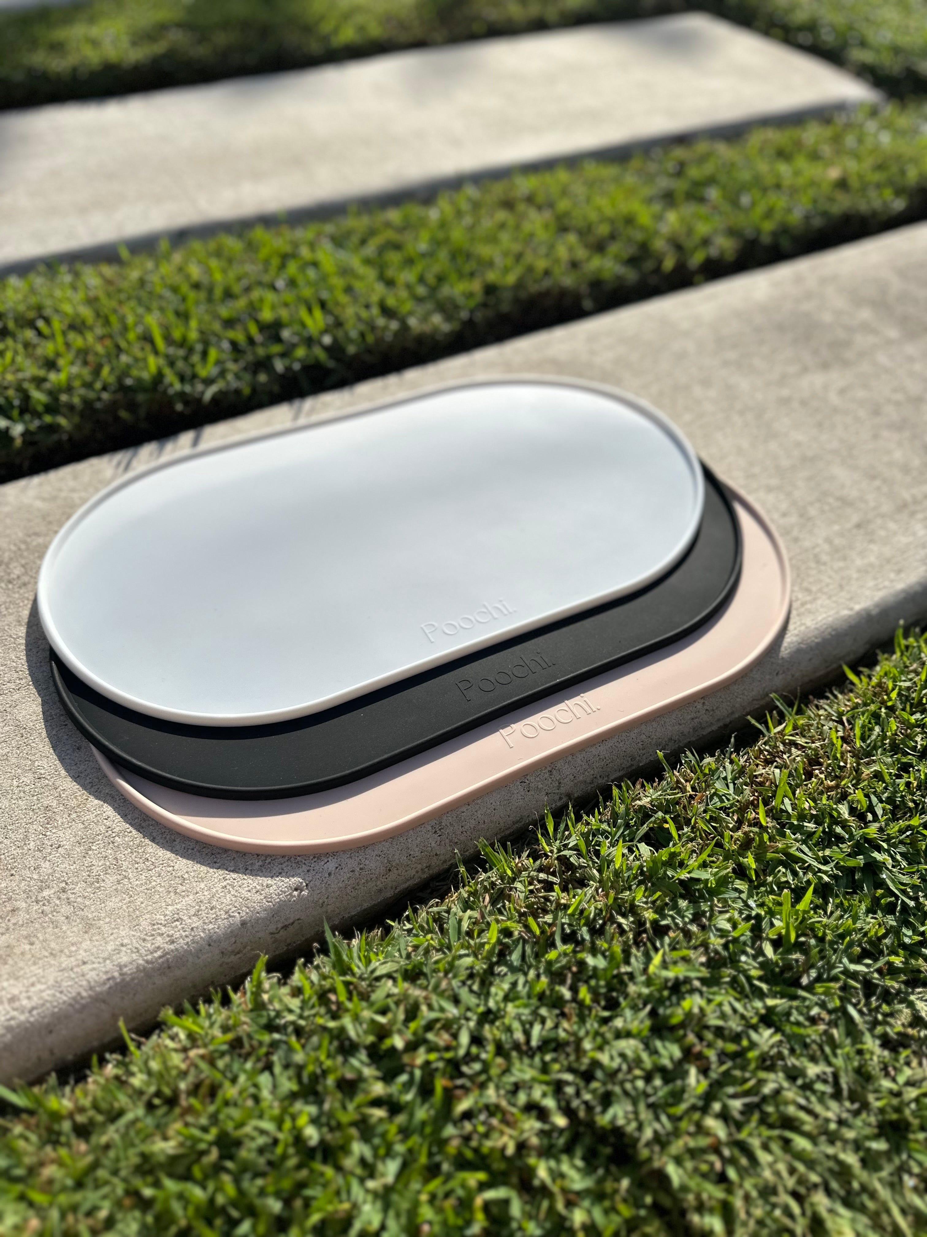 A stack of silicone feeding mats for pets such as dogs or cats. The mat comes in three colours such as black, white and beige