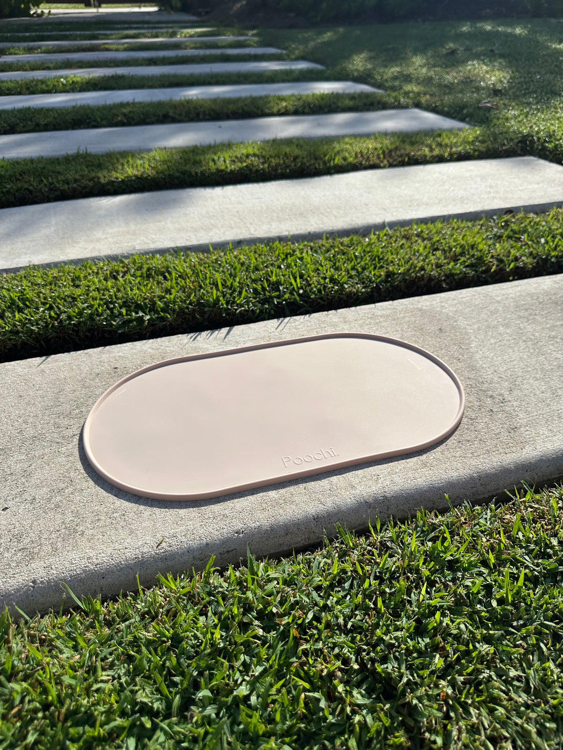 A beige silicone feeding mat placed outside on the concrete in the sun, branded Poochi. 