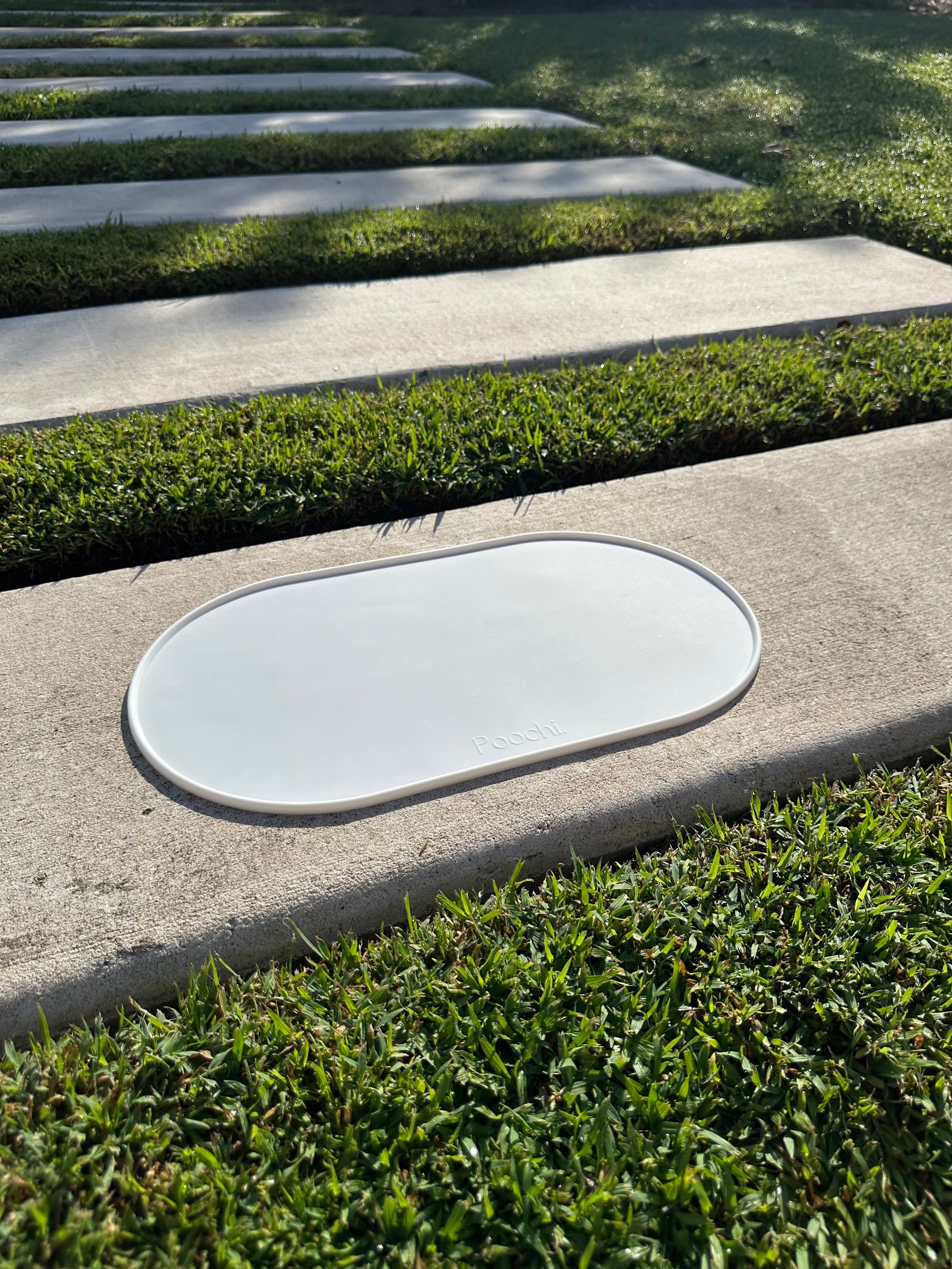 A white silicone feeding mat placed outside on the concrete in the sun, branded Poochi. 