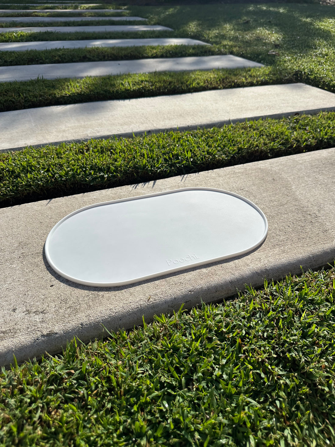 A white silicone feeding mat placed outside on the concrete in the sun, branded Poochi. 